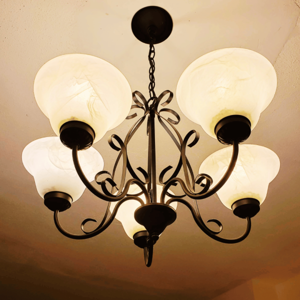 Ironwork chandelier with upward-facing, frosted-glass sconces which bounce light off ceiling
