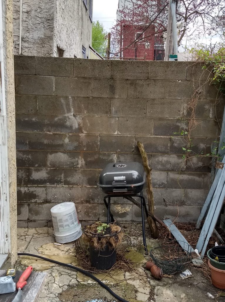Gray cinder block wall and broken concrete patio with broken grill