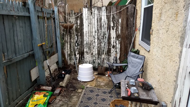 Broken fence with peeling paint, concrete patio with folding camp chair and outdoor rug